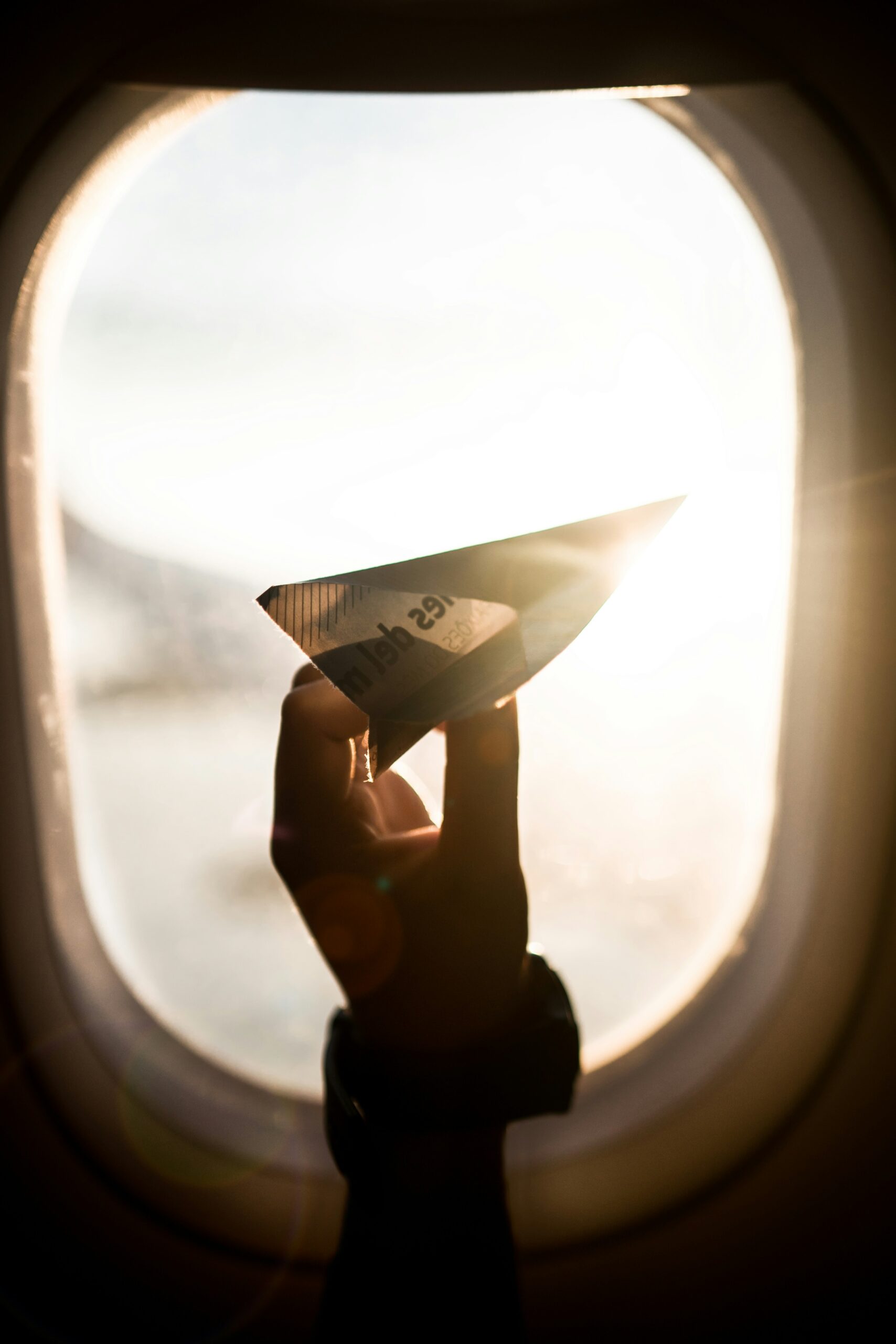 hand holding paper airplane in front of plane window